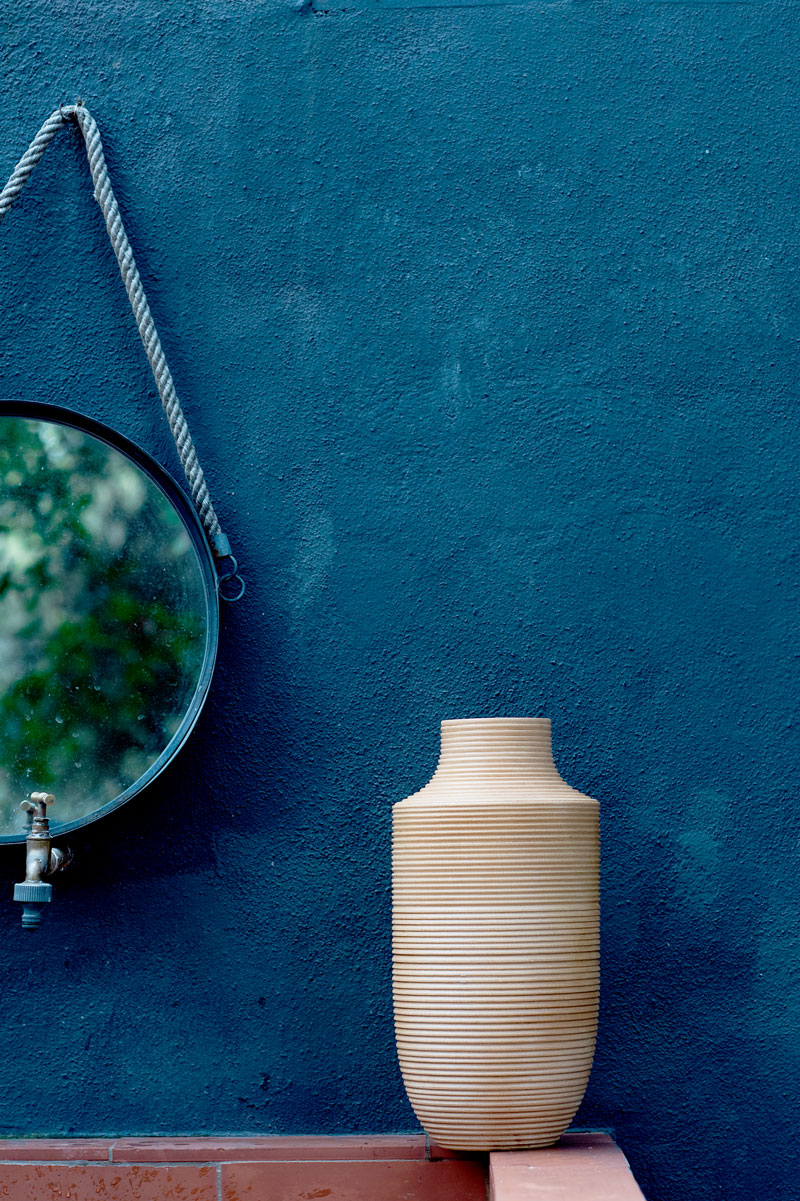 Decorative vase with textured design beside a round mirror on a blue wall, enhancing interior aesthetics for home improvement projects.